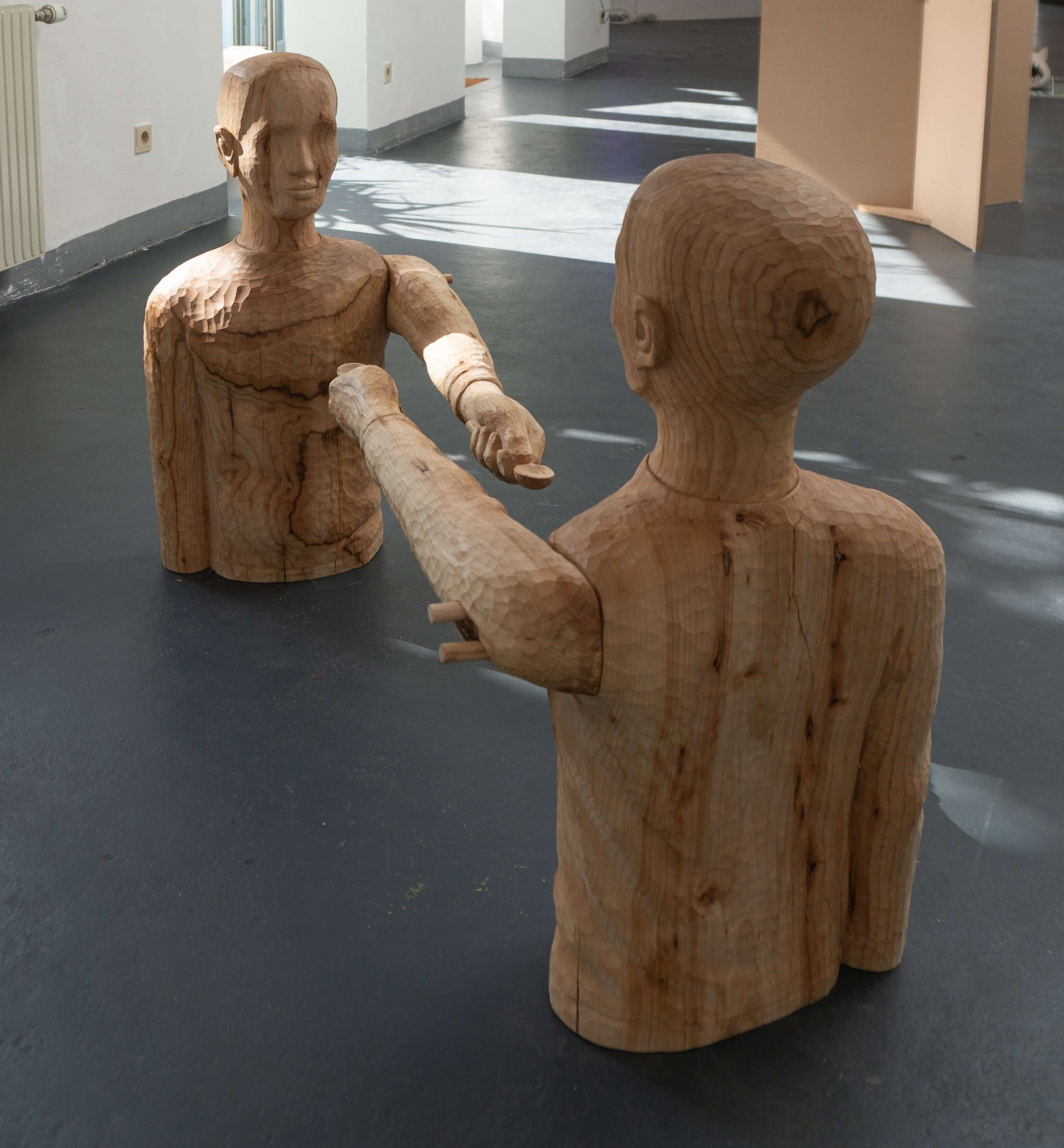 Wooden sculpture of two bodies holding a spoon.