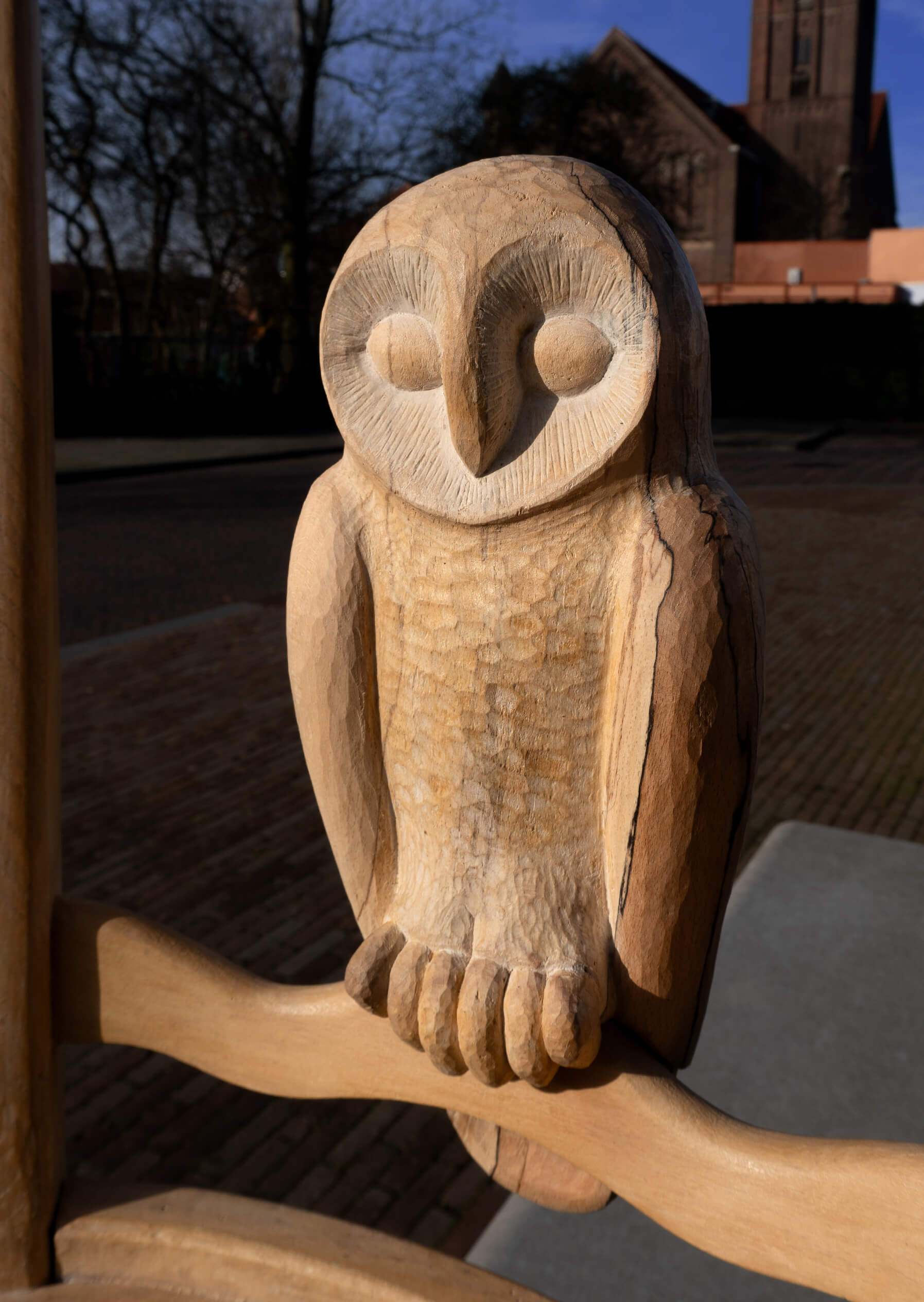 Detail of a wood sculpture depicting a bird (owl) and a chair. The photo is taken outside with evening light.
